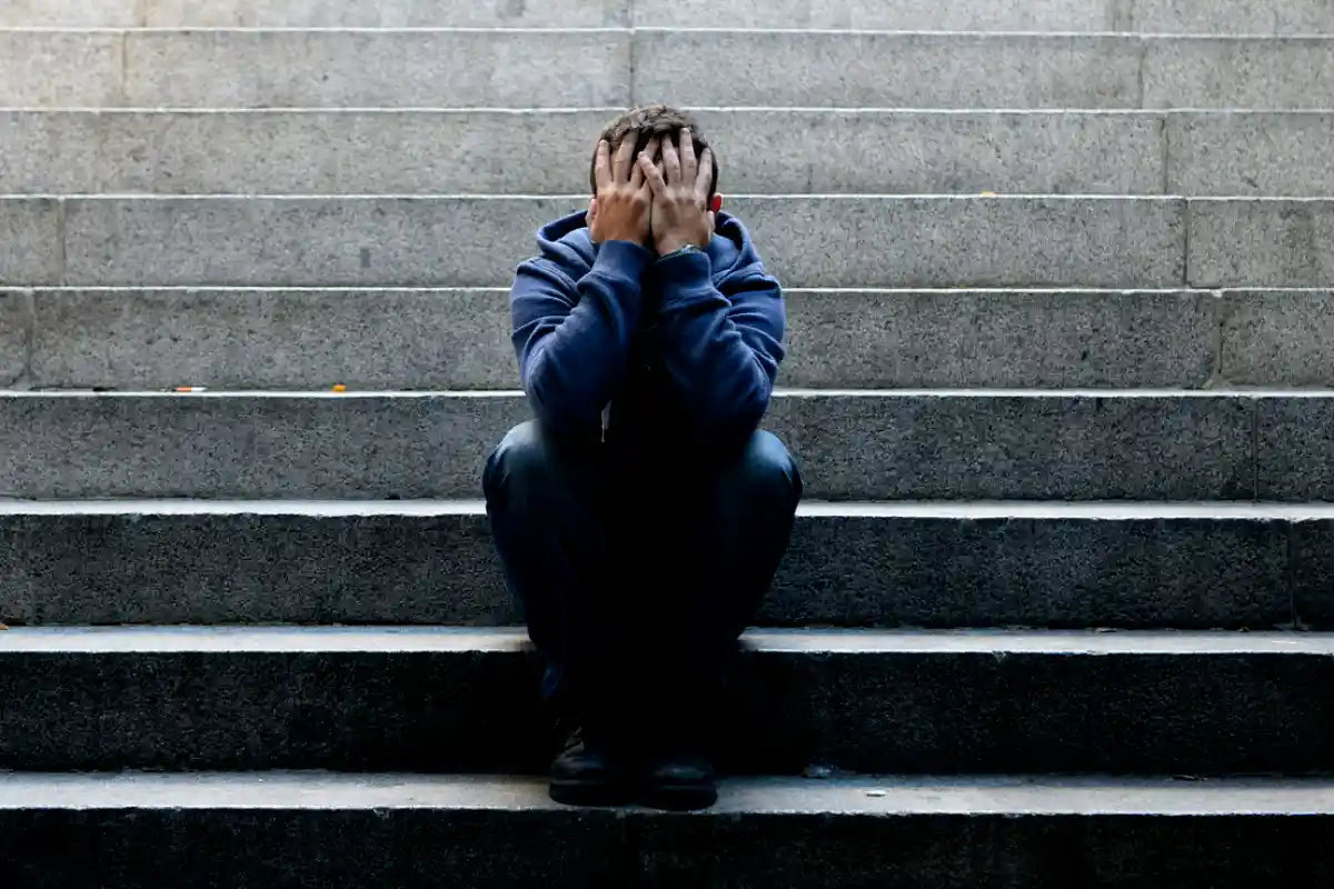 man sitting on stairs in a public area covering his face and facing anxiety