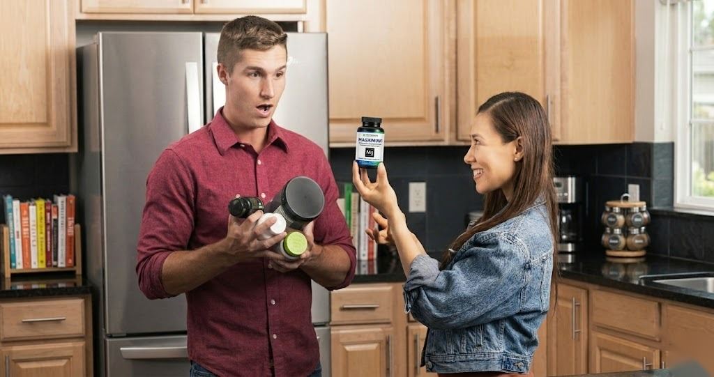Woman holding one bottle of Trio Nutrition Magximum while a man holds several separate supplement bottles