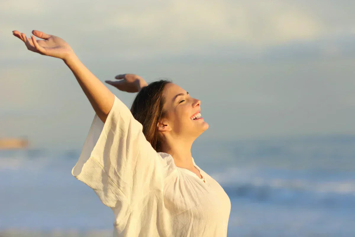 woman at the beach holding her arms up and smiling, feeling the effects of taking a calming magnesium supplement