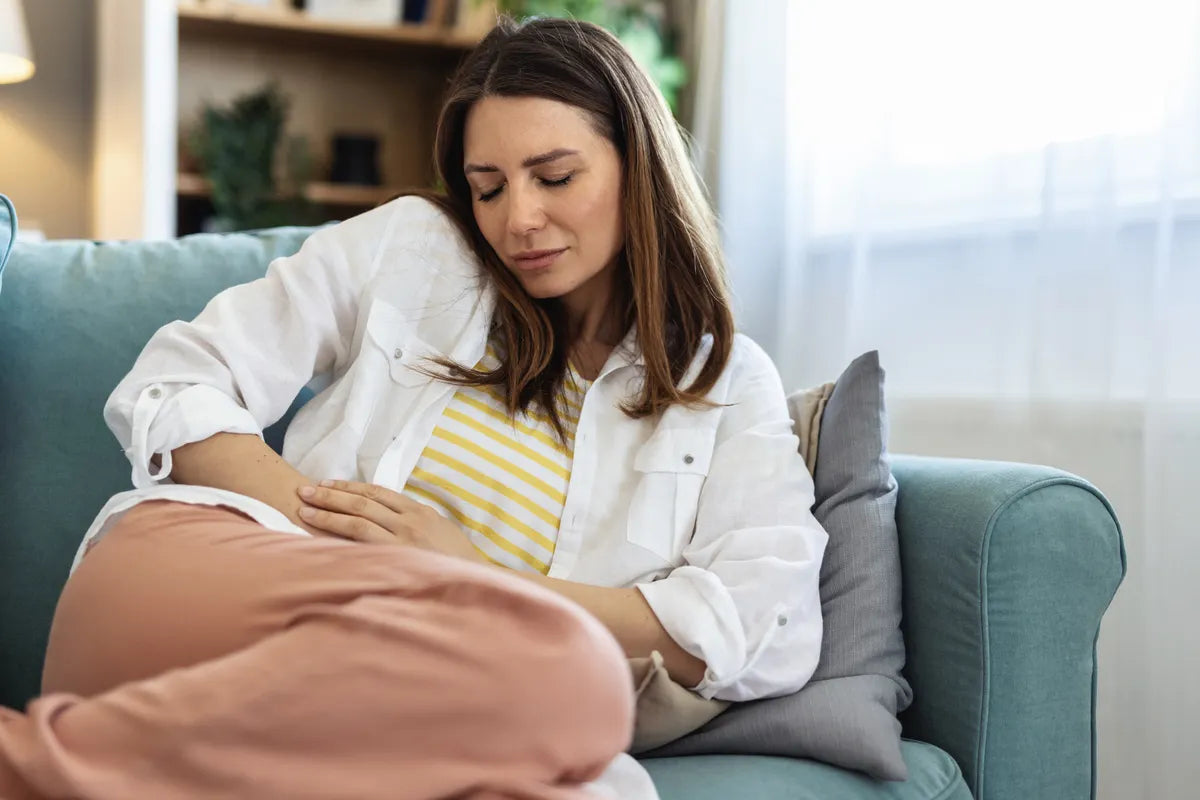 woman on her couch holding her tummy while closing her eyes, suffering from bloating