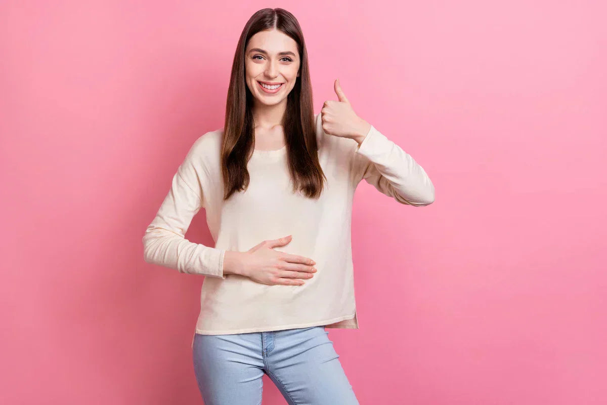 Smiling woman giving a thumbs-up while touching her stomach.