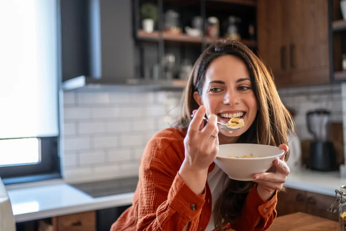 woman about to eat a spoonful of cereal while holding the bowl iand leaning in her kitchen table