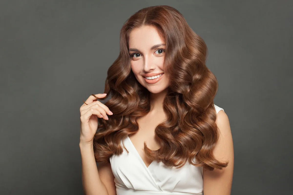 a brunette holding her healthy long, think, and curly hair while smiling at the camera
