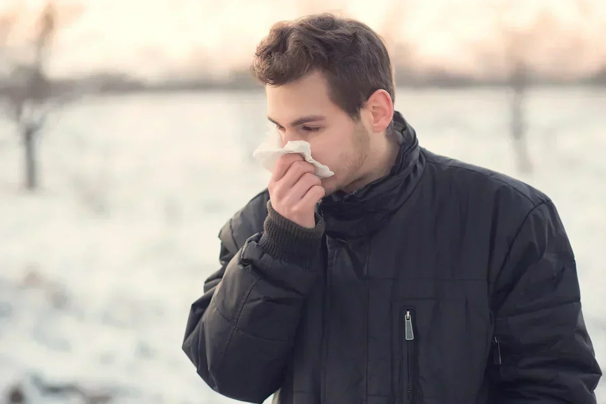 man suffering from cold and blowing his nose during the winter