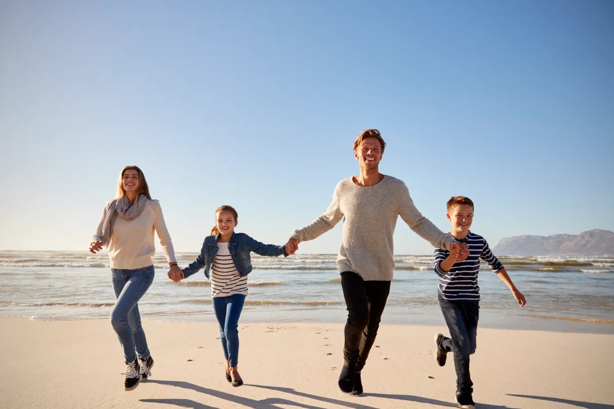 a family of four holding each other's hands at the beach with mom, dad, son, and daughter smiling happily at the camera