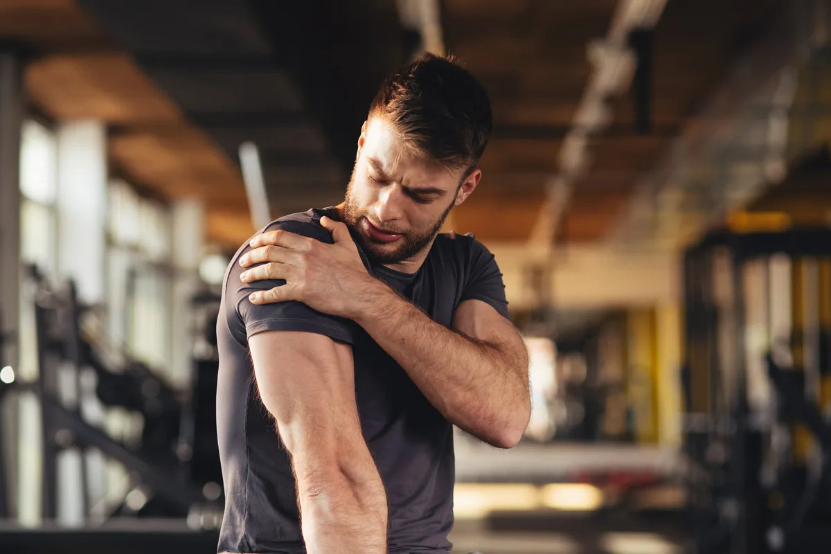 man at the gym holding his arms due to soreness